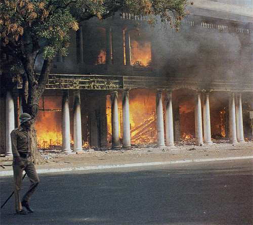 After the outbreak of rioting, a policeman walks past burning shops in downtown New Delhi.